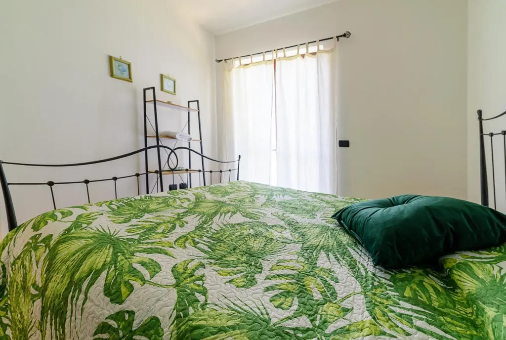 Green tropical bedroom: double room at Villa MaLuGio with green tropical bedspread, wrought-iron bed and white curtains, Casal Velino Cilento