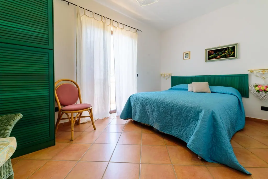 Bedroom with balcony: double room at Villa MaLuGio with green headboard, white curtains and balcony access, Casal Velino Cilento